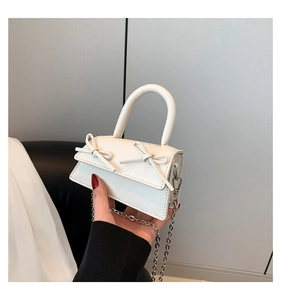 Close-up of white mini handbag with bow accents and silver metal chain strap