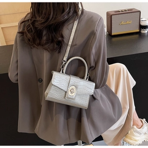 Detail shot of a silver crocodile-pattern crossbody bag with metal twist-lock and top handle