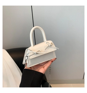 Detail of a creamy white mini handbag featuring two cute bows and a silver metal chain