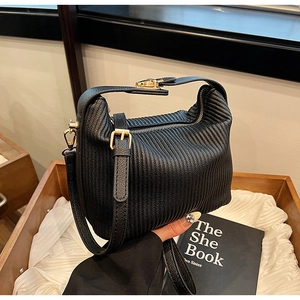 Détail d'un sac plissé noir avec ferrures dorées dans un présentoir en bois chic