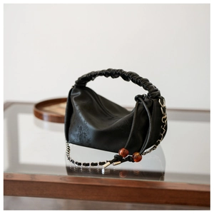Détail d'un sac à main plissé noir avec gaufrage feuilles de bambou et perles ambrées