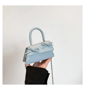 Close-up of light blue mini handbag featuring glossy patent leather and twin bow details