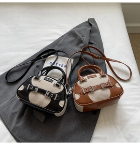 Detail of two-tone canvas and leather crossbody bags with metal buckles on a grey blazer