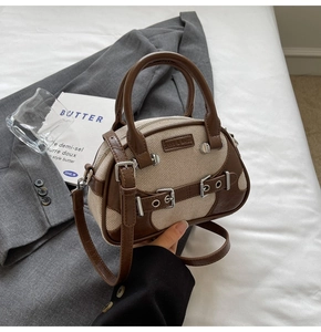 Detail of retro canvas handbag with brown leather trim and silver buckles on a bed