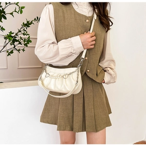 Détail du sac plissé blanc avec pendentif cœur en métal et chaîne de perles décorative