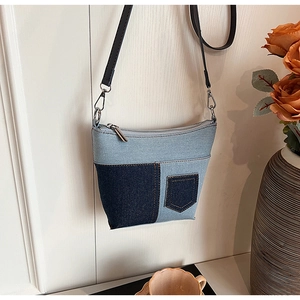 Detail einer blauen Denim-Umhängetasche mit dunkler Tasche und schwarzem Lederriemen