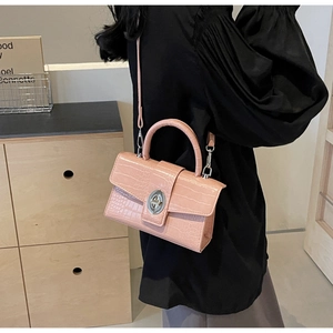 Pink crocodile-textured handbag with silver oval twist lock worn as a crossbody bag
