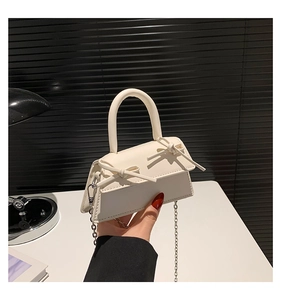 Detail of cream white mini crossbody bag featuring dual bow accents and silver chain strap