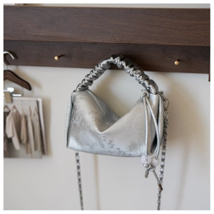 Gros plan d'un sac en satin gris argenté avec motifs bambou et poignée plissée