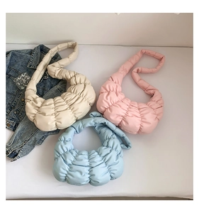 Detailed flat lay of pleated crescent bags in beige, pink, and blue showing quilted texture