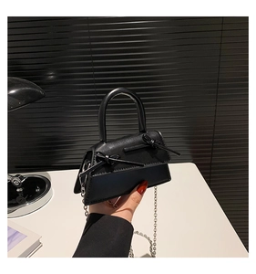 Detail of minimalist black trapezoid handbag with dual bow accents and silver chain strap