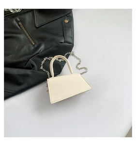 Top-down view of a cream mini handbag with silver chain strap beside a black leather jacket