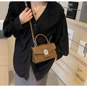 Brown crocodile texture handbag detail featuring a silver turn-lock and adjustable strap