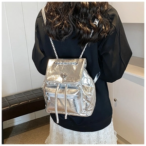 Detail of silver quilted backpack featuring heart lock and metal chain straps on model