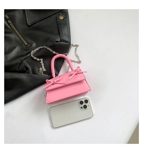 Mini pink crossbody bag with bow details and metal chain, shown with phone for size scale
