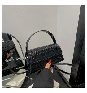 Detail of black faux crocodile leather handbag with glossy finish and silver buckle