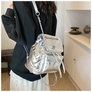 Detail of silver quilted backpack featuring a metallic chain strap and heart ornament