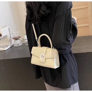 Detail of beige crocodile pattern handbag with silver swivel lock on black shirt