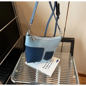 Detail der blauen Denim-Patchwork-Umhängetasche mit Kontrastnähten auf einem Metallstuhl