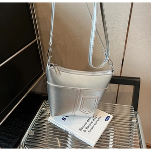 Detail der silbernen Metallic-Schultertasche mit Kontrastnaht auf Büchern und Stuhl