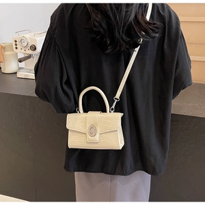 Detail of a chic off-white crocodile embossed small square bag worn over the shoulder