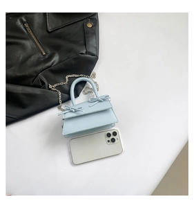 Mini light blue handbag with bow detail and silver chain strap next to a smartphone