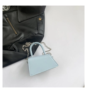 Detail of light blue mini trapezoid handbag with thick top handle and silver chain strap