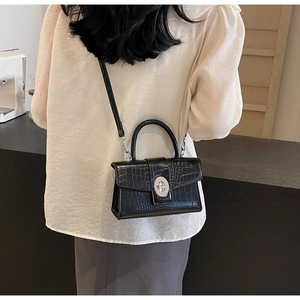 Detail of black crocodile pattern crossbody bag with silver twist lock and handle