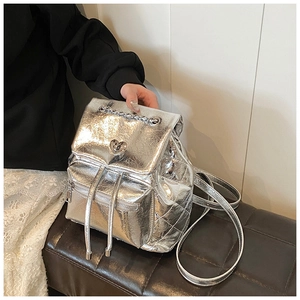 Detail of silver metallic backpack featuring a heart-shaped turn-lock and chain strap