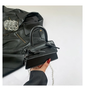 Detail of a black ballet-style mini bag with bow accents and silver chain strap