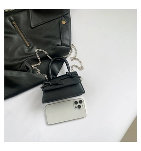 Top view of mini black crossbody bag with bow details next to a white smartphone