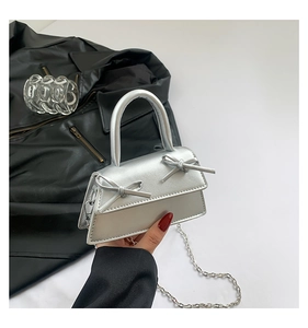 Detail of silver mini trapezoid bag with dual bow accents and metallic chain strap