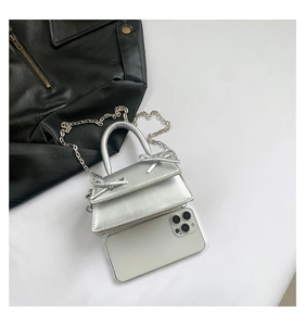 Detail of silver mini trapezoid bag with bows and metal chain next to a smartphone