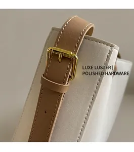 Dettaglio della tracolla in pelle marrone con fibbia dorata su borsa a secchiello