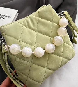 Détail du sac seau matelassé vert clair avec une grande poignée en perles et texture fine