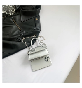 Mini silver handbag with double bows and chain strap shown next to a smartphone