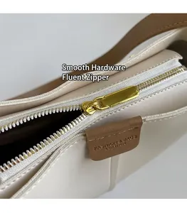 Dettaglio della cerniera in metallo dorato e tag in pelle sulla borsa a secchiello color crema