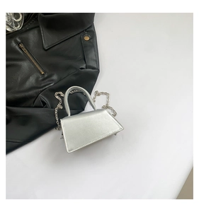 Detail of silver mini trapezoid bag with metal chain strap on a black leather jacket