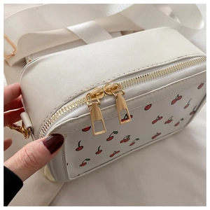 Primer plano de bolso bandolera blanco con estampado de cerezas y cremalleras doradas