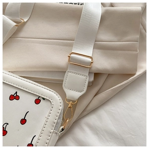 Detalle del bolso con estampado de cerezas, correa de tela y ganchos de metal dorado