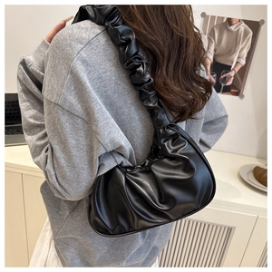 Detail of black pleated cloud bag with ruched strap worn by a model in a cozy room