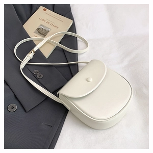 Detail of a minimalist cream saddle bag with adjustable strap and tonal round buckle closure