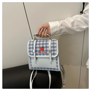 Detail of blue plaid backpack with apple embroidery and top handle held by a model