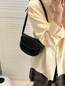 Elegant black leather saddle bag for women shown as a stylish crossbody on model