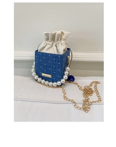 Detailed macro of denim bucket bag showing diamond quilt texture and pearl handle