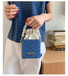 Detail of blue denim bucket bag featuring large pearl handle and drawstring closure