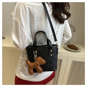 Detalle del bolso negro con relieve de mariposa y colgante de perro en modelo