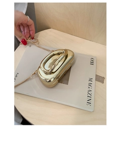 Macro detail of glossy gold mirrored evening bag with streamline handle and metal chain