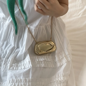 Detailed macro of gold lava-shaped metallic mini bag with mirror finish and slim chain strap