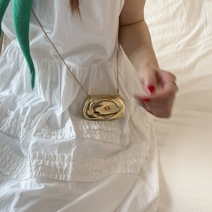 Detailed macro view of the gold mini metal bag with artistic wave texture and chain strap